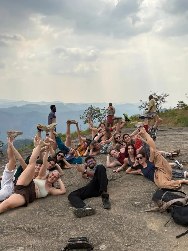 Retreat group doing playful yoga poses on a rocky hilltop